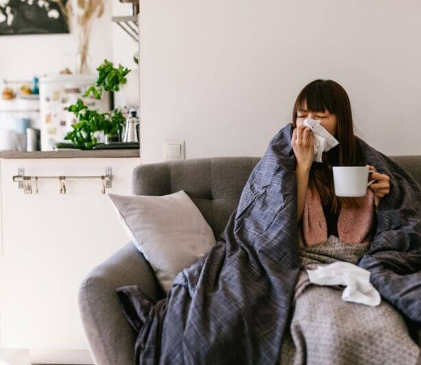 treating seasonal allergies with TCM herbal formulas - woman on couch with blanket blowing her nose and holding mug